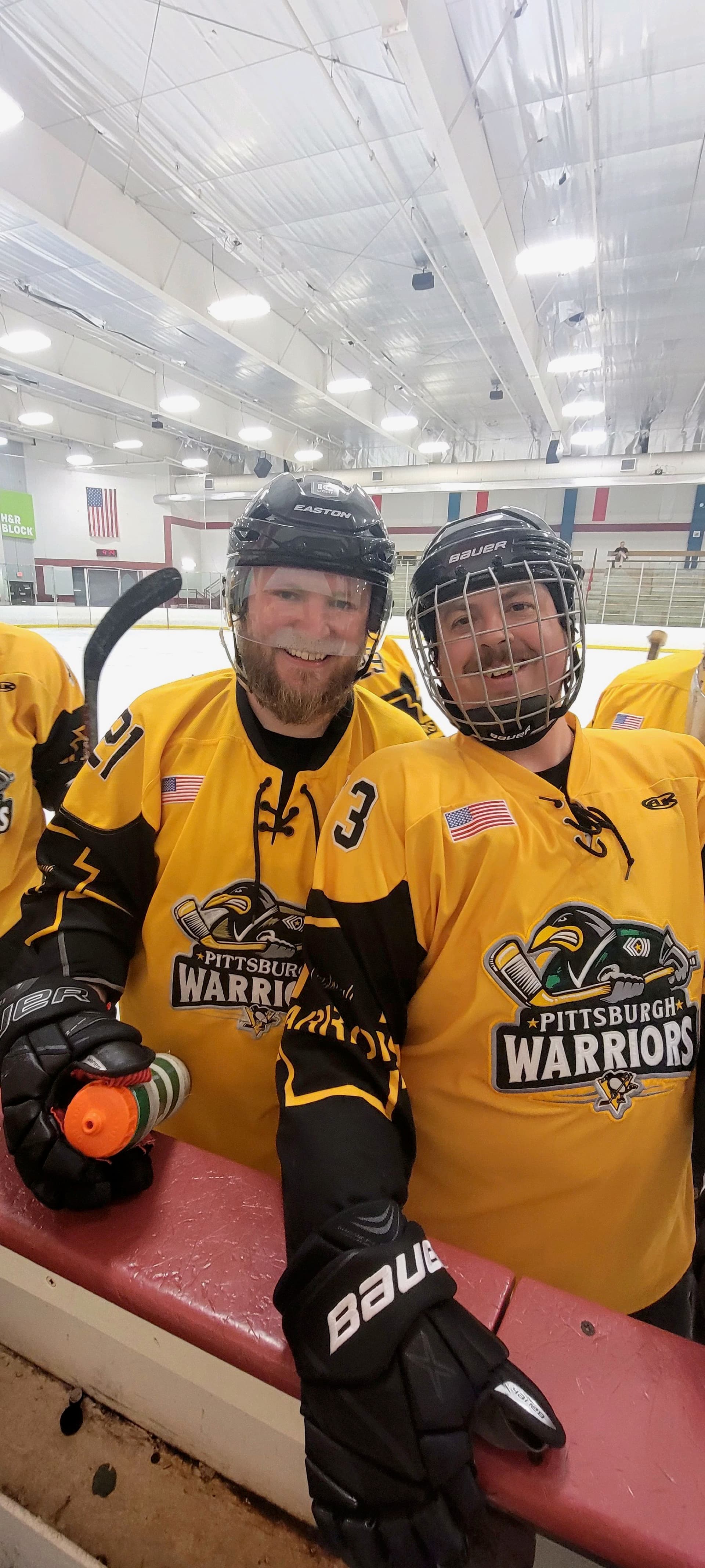 Two Pittsburgh Warriors players smiling on the bench after skating together.